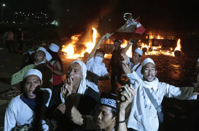 Muslim protesters chant slogans near burning police trucks during a clash with the police outside the presidential palace in Jakarta, Indonesia, Friday, November 4, 2016. Police in the Indonesian capital clashed with hard-line Muslim protesters refusing to disperse after a massive protest Friday to demand the arrest of the city's minority-Christian governor for alleged blasphemy. (Photo by Dita Alangkara/AP Photo)