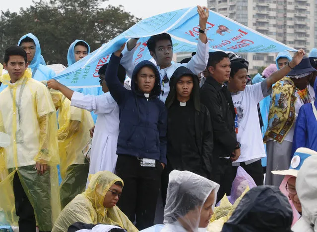People shield themselves from the rain as they gather at Rizal Park to attend a mass by Pope Francis in Manila January 18, 2015. (Photo by Erik De Castro/Reuters)