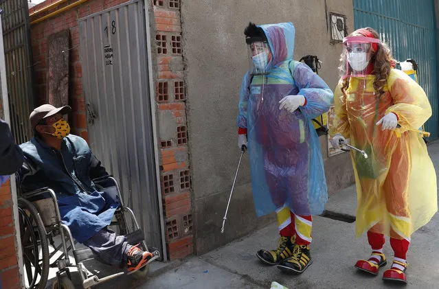 Clowns Perlita and Tapetito, wearing protective gear amid the new coronavirus pandemic, speak with resident Enrique Zeballos as they arrive to disinfect his home free of charge, in El Alto, Bolivia, Friday, September 11, 2020. The lack of traditional employment for the clowns due to the pandemic has led them towards other avenues of making money. But for people with limited income they provide their disinfection services free of charge. (Photo by Juan Karita/AP Photo)