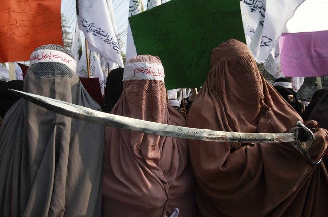 A burqa clad woman (R) supporter of religious group Tehreek-e-Sirate Mustaqeem, holds a sword, as she joins others in a protest against satirical French weekly newspaper Charlie Hebdo, which featured a cartoon of the Prophet Mohammad as the cover of its first edition since an attack by Islamist gunmen, in Lahore January 20, 2015. Arabic writing on sword reads, “There is no god but Allah, and Mohammad is his Prophet”. (Photo by Mohsin Raza/Reuters)