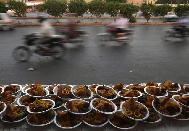 Pakistan motorcyclists ride past plates of Iftar foods placed for residents to break their fast along a street in Karachi on May 29, 2017. Muslims throughout the world are marking the month of Ramadan, the holiest month in the Islamic calendar during which Muslims fast from dawn until dusk. (Photo by Asif Hassan/AFP Photo)