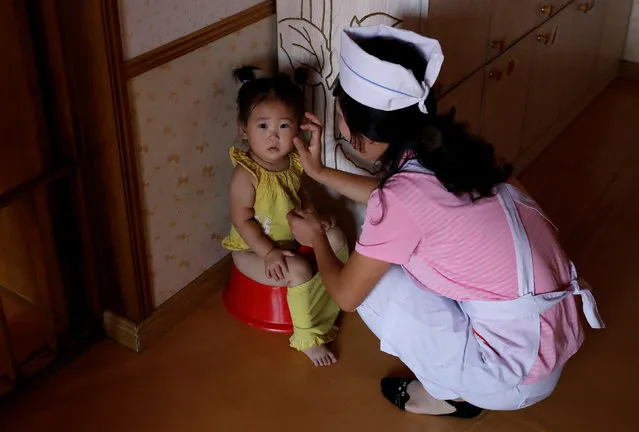 A girl is helped by a caretaker at kindergarten and daycare for employees' children at a silk factory during a government organised visit for foreign reporters ahead of the 70th anniversary of North Korea's foundation in Pyongyang, North Korea on September 7, 2018. (Photo by Danish Siddiqui/Reuters)