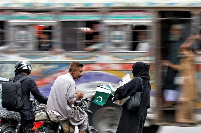 A woman speaks with a customer while selling national flags, ahead of Pakistan's Independence Day, along a road in Karachi, Pakistan on August 10, 2023. (Photo by Akhtar Soomro/Reuters)