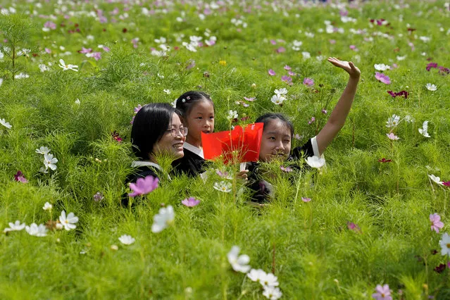 A woman and two girls, one holding Chinese flags, pose in a flower field on the country's 74th National Day in Hangzhou, China, Sunday, October 1, 2023. (Photo by Aijaz Rahi/AP Photo)