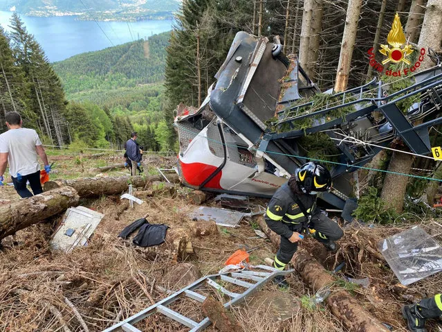 Rescuers work by the wreckage of a cable car after it collapsed near the summit of the Stresa-Mottarone line in the Piedmont region, northern Italy, Sunday, May 23, 2021. A cable car taking visitors to a mountaintop view of some of northern Italy's most picturesque lakes plummeted to the ground Sunday and then tumbled down the slope, killing at least 13 people and sending two children to the hospital, authorities said. (Photo by Italian Vigili del Fuoco Firefighters via AP Photo)