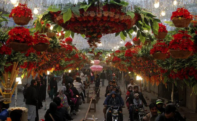 Motorcyclists drive through a street decorated with flowers on the eve of celebrations marking the birth of Islam's Prophet Muhammad, in Lahore, Pakistan, Monday, December 12, 2016. Pakistani Muslims celebrate the holiday Monday with religious processions, ceremonies and by distributing free meals to the poor. (Photo by K.M. Chaudary/AP Photo)