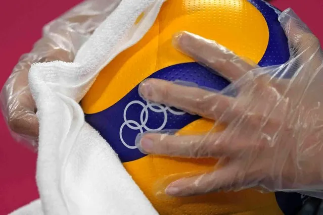 A steward uses a plastic glove and a cloth to disinfect a volleyball ball during a rehearsal for the start of the volleyball preliminaries at Ariake Arena during the 2020 Summer Olympics, Friday, July 23, 2021, in Tokyo, Japan. (Photo by Frank Augstein/AP Photo)