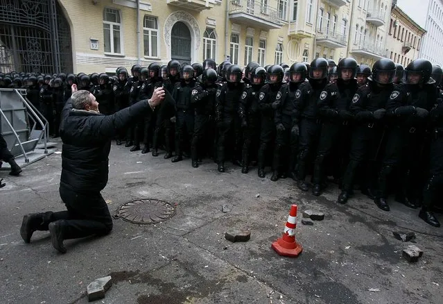 A man kneels down while police stand guard near the presidential administration building during a rally held by supporters of EU integration in Kiev, on December 1, 2013. Ukraine's interior minister warned tens of thousands of protesters starting a pro-Europe rally in the capital that police would respond if there were mass disturbances. (Photo by Gleb Garanich/Reuters)