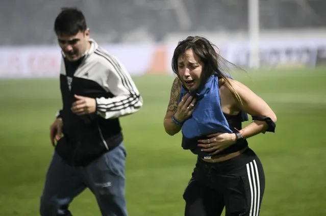 Fans of Gimnasia de La Plata choke on tear gas during a local tournament match between Gimnasia de La Plata and Boca Juniors in La Plata, Argentina, Thursday, October 6, 2022. The match was suspended after tear gas thrown by the police outside the stadium wafted inside affecting the players as well as fans who fled to the field to avoid its effects. (Photo by Gustavo Garello/AP Photo)