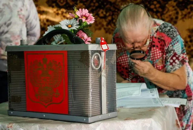 A woman looks through a ballot before casting a vote in her house as members of an electoral commission visit local residents during a three-day parliamentary election in Tarbagatay village in the Republic of Buryatia, Russia on September 17, 2021. (Photo by Maxim Shemetov/Reuters)