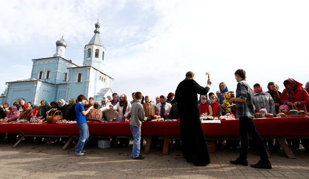 An Orthodox priest sprinkles holy water on believers and their “paskha” cakes, eggs and other food on the eve of Orthodox Easter outside the church in the town of Bobruisk, Belarus, April 30, 2016. (Photo by Vasily Fedosenko/Reuters)