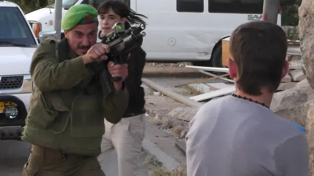 In this image taken from video obtained from Youth Against Settlements, a group of Palestinian activists, which has been authenticated based on its contents and other AP reporting, an Israeli soldier points his gun at a Palestinian teen in the West Bank city of Hebron. The reprimand of an Israeli soldier – caught on video cursing and pointing a cocked gun toward the head of a Palestinian teen – has triggered the biggest outpouring of frustration by Israeli soldiers in years about their service in the West Bank. (Photo by AP Photo/Youth Against Settlements)