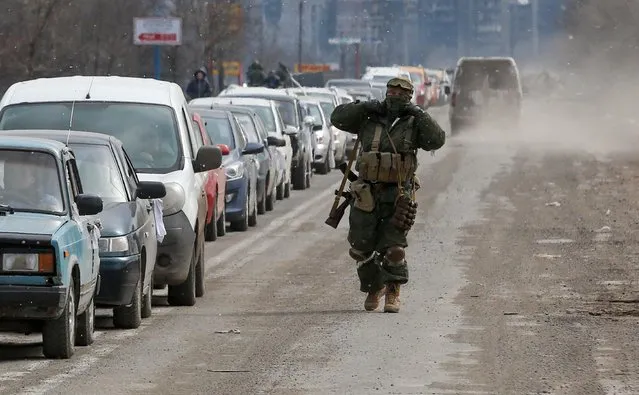 A service member of pro-Russian troops walks near a line of cars with evacuees, who leave the besieged southern port city of Mariupol, Ukraine on March 17, 2022. (Photo by Alexander Ermochenko/Reuters)