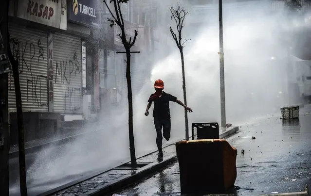 A protester runs away as Turkish riot police use water cannons to disperse protesters during a demonstration against the recent mine accident in Soma, on May 22, 2014, in the Okmeydani district of Istanbul. One man was injured when Turkish riot police today fired tear gas and water cannon to disperse a group of Istanbul protesters hurling Molotov cocktails and stones. (Photo by Bulent Kilic/AFP Photo)