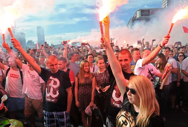 People stand on the city's main intersection holding burning flares to commemorate the 71st anniversary of the 1944 Warsaw Uprising in Warsaw, Poland, Saturday, August 1, 2015. Thousands of young city residents opened an uneven struggle on August 1, 1944 in an effort to liberate the city from the Nazis and take control ahead of the advancing Soviet Red Army. The poorly armed fighters held on for 63 days against the overpowering German troops. Some 200,000 fighters and residents were killed and the Nazis razed the city. (Photo by Alik Keplicz/AP Photo)