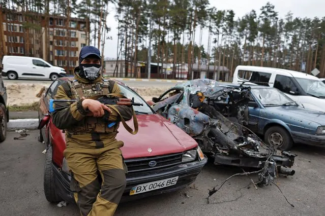 A member of the Ukrainian Territorial Defence Forces sits next to a destroyed car, amid Russia's attack on Ukraine, in Irpin, Kyiv region, Ukraine on April 18, 2022. (Photo by Zohra Bensemra/Reuters)