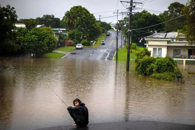 Jai Connors fishes in rising floodwater from the swollen Bremer river in front of home in West Ipswich, Australia's Queensland state on February 26, 2022. (Photo by Patrick Hamilton/AFP Photo)