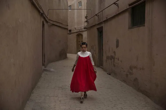 A Uyghur woman wearing a gown for the Eid holiday walks from her house on July 30, 2014 in old Kashgar, Xinjiang Province, China. (Photo by Kevin Frayer/Getty Images)