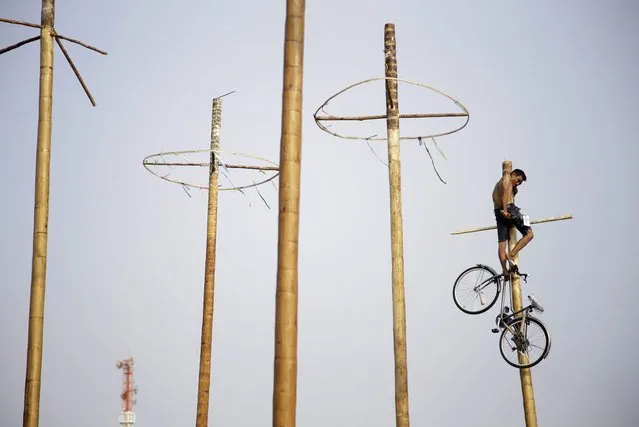 A participant uses his feet to lower a bicycle down from the top of a greased-pole during a greased-pole climbing competition held as a part of the Independence Day celebrations in Jakarta, Indonesia, Sunday, August 17, 2014. (Photo by Dita Alangkara/AP Photo)