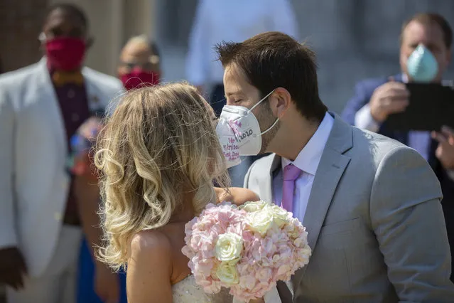 Gabrielle Schmees, 29, and Diego Grassano, 31, kiss wearing protective masks on the day of their wedding at the Gerald D. Hines Waterwall Park on Monday, April 27, 2020, in Houston. Because of COVID-19, the couple decided to postpone their official wedding and have a small one at the Waterwall Park until December when they can have the official one with all of their family and friends. (Photo by Marie De Jesus/Houston Chronicle via AP Photo)