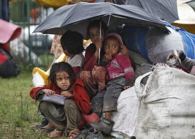 Kashmiri children with their belongings sit under an umbrella during rain in Srinagar September 6, 2014. Authorities declared a disaster alert in the northern region after heavy rain hit villages across the Kashmir valley, causing the worst flooding in two decades. (Photo by Danish Ismail/Reuters)