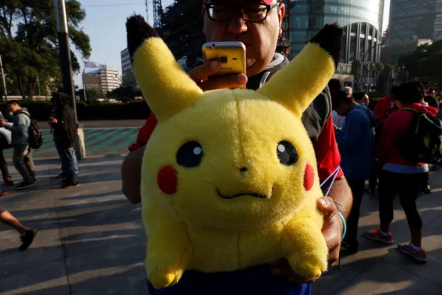 A man carries stuffed toy of a character from Pokemon, Pikachu, as he plays Pokemon Go during a gathering to celebrate “Pokemon Day” in Mexico City, Mexico August 21, 2016. (Photo by Carlos Jasso/Reuters)