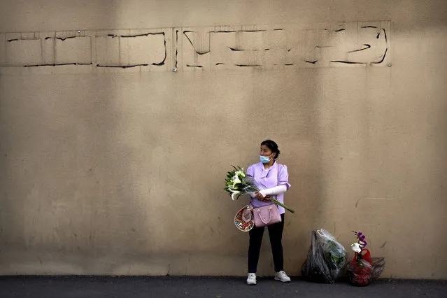A woman holding bags of fresh flowers wears a face mask to protect against the coronavirus as she stands outside a market in Beijing, Saturday, August 22, 2020. Authorities in China's capital announced on Thursday that masks would no longer be mandatory outdoors as a virus outbreak in the country's northwestern region of Xinjiang appears to have been brought under control. (Photo by Mark Schiefelbein/AP Photo)