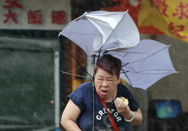 A woman eats and struggles with her umbrella against powerful gusts of wind generated by typhoon Megi across the the island in Taipei, Taiwan, Tuesday, September 27, 2016. Schools and offices have been closed on Taiwan and people in dangerous areas have been evacuated as a large typhoon with 162 kilometers (100 miles) per-hour winds approaches the island. (Photo by Chiang Ying-ying/AP Photo)