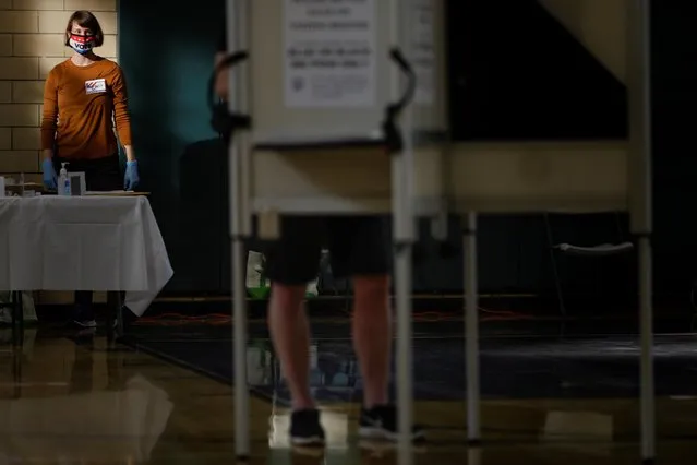 Ballot clerk Chris Biles looks on through a plexiglass barrier while wearing personal protective equipment at the School Without Walls at Francis-Stevens voting station in Washington, U.S., on October 28, 2020. (Photo by Tom Brenner/Reuters)
