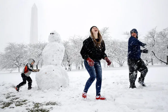 Dane Lariscy, 5, left, works on a snowman as his siblings, Amanda Lariscy, 17, and Blaze Lariscy, 15, laugh while having a snowball fight on the National Mall during the Ochlockonee, Fla., family's first snowfall, Wednesday, March 21, 2018, during a spring snowstorm in Washington. Their parents decided to wait out the storm instead of trying to drive to Florida in the snow. (Photo by Jacquelyn Martin/AP Photo)