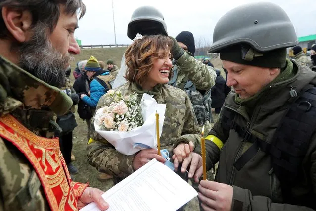 Members of the Ukrainian Territorial Defence Forces Lesia Ivashchenko and Valerii Fylymonov exchange rings at their wedding during Ukraine-Russia conflict, at a checkpoint in Kyiv, Ukraine on March 6, 2022. (Photo by Mykola Tymchenko/Reuters)