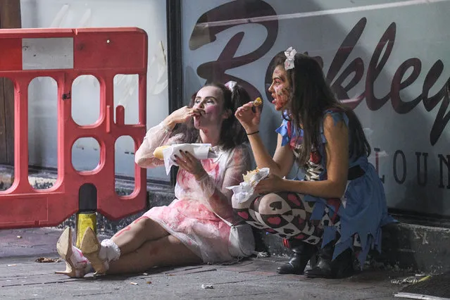 Two friends in fancy dress eat food after a night of partying on UK Birminghams Broad Street during the night of Halloween on October 30, 2016. It was nightmare on Broad Street last night as thousands of revellers hit the streets for Halloween. Party-goers in Birmingham, West Mids, could be seen collapsed on the floor as paramedics tended to them while another appeared to urinate against a wall. Another guy, dressed in camouflage, was violently sick on the street and a girl was also crouched over vomiting as her friend comforted her. Students went all out with their fancy dress as part of the Nightmare on Broad Street event, which saw over 4,500 people hit the citys infamous strip. (Photo by Caters News Agency)