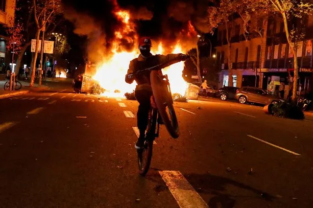 A person rides a bicycle in front of a fire during a protest against the closure of bars and gyms, amidst the coronavirus disease (COVID-19) outbreak, in Barcelona, Spain on October 30, 2020. (Photo by Nacho Doce/Reuters)