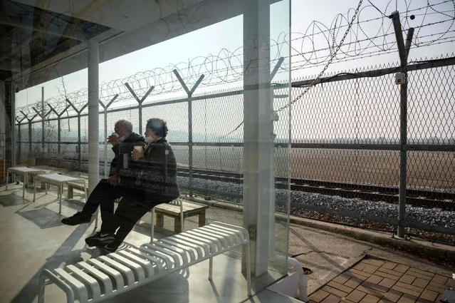 An elderly couple drink coffee before a barbed wire fence at the Imjingak tourist park beside the civilian buffer zone that leads to the Demilitarized Zone (DMZ) separating North and South Korea, in Paju, north of Seoul on February 12, 2021. (Photo by Ed Jones/AFP Photo)