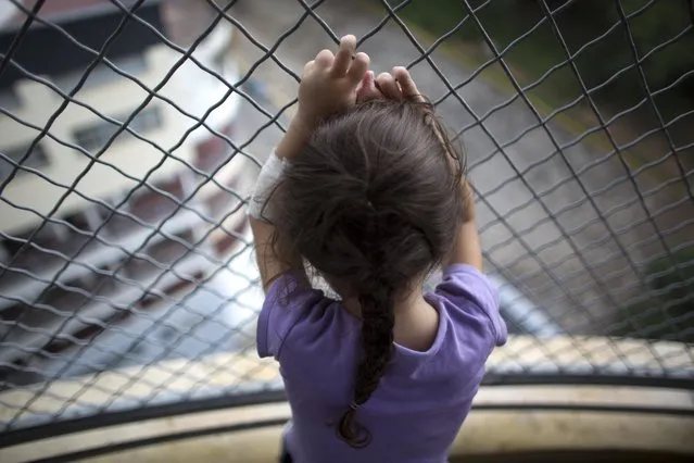 In this August 23, 2016 photo, 3-year-old Ashley Pacheco hooks her fingers around the links of a fence as she gazes out from a hospital balcony, at University Hospital, in Caracas, Venezuela. This is the only place Ashley is able to breathe in fresh air. A scraped knee in mid-July led to a staph infection. There were not enough antibiotics to treat the infection, and so Ashley was kept in the public hospital for two months. (Photo by Ariana Cubillos/AP Photo)