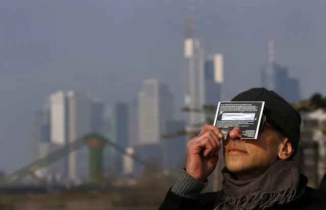 A man watches a partial solar eclipse looking through a protection foil shield as he sits on the terrace of a restaurant at the bank of river Main in front of the skyline of Frankfurt, March 20, 2015. (Photo by Kai Pfaffenbach/Reuters)