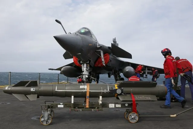 Red jacket ordnance crew place bombs under a Rafale fighter jet aboard France's Charles de Gaulle aircraft carrier on mission in the Gulf, January 28, 2016. (Photo by Philippe Wojazer/Reuters)