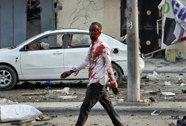 An injured civilian walks away from the scene after being wounded in a bomb blast near the Sahafi hotel in the capital Mogadishu, Somalia, Friday, November 9, 2018. Three car bombs by Islamic extremists exploded outside the hotel, which is located across the street from the police Criminal Investigations Department, killing at least 10 people according to police. (Photo by Farah Abdi Warsameh/AP Photo)