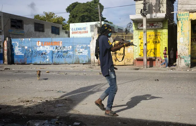 An armed civilian carries a weapon on during a shootout between rival gangs to take control of the Croix-des-Bossales market, on Boulevard Jean-Jacques Dessalines, a main commercial artery, in Port-au-Prince, Haiti, Wednesday, November 21, 2018. The fight for control of the market, where vendors pay the controlling gang regular payments, erupted amid days of protests and a strike against alleged government corruption. (Photo by Dieu Nalio Chery/AP Photo)