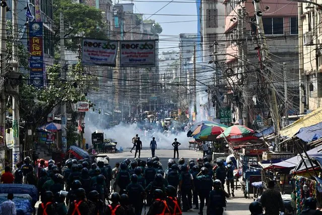 Bangladesh police (foreground) stand guard along a road during clashes with garment workers (top) protesting to demand the increase of their salaries, in Dhaka on November 2, 2023. Hundreds of garment factories in Bangladesh have shuttered as thousands of workers staged violent protests to demand a near-tripling of their wages, police said on November 2. (Photo by Munir Uz Zaman/AFP Photo)
