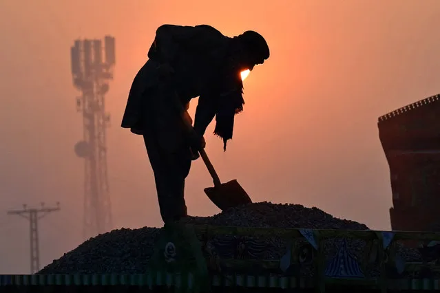 A labourer is silhouetted against the rising sun amid smoggy conditions in Lahore on November 14, 2023. (Photo by Arif Ali/AFP Photo)