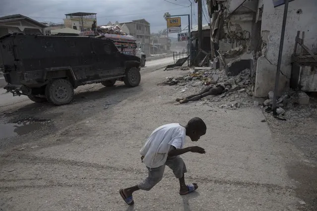 A boy crouches to avoid the camera as he runs past the body of a man killed during clashes between police and gang members, in the Martissant neighborhood of Port-au-Prince, Haiti, Saturday, October 2, 2021. Haitian gangs have seized control of more land and committed more crimes than ever before – all without a care. (Photo by Rodrigo Abd/AP Photo)