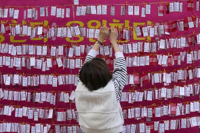 A woman hangs a paper note to wish for her child's success during a special service on the eve of the college entrance exam at the Jogyesa Buddhist temple in Seoul, South Korea, Wednesday, November 17, 2021. About 500,000 high school seniors and graduates across the country are expected to take the College Scholastic Ability Test. (Photo by Ahn Young-joon/AP Photo)