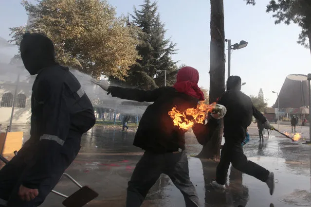 A masked demonstrator readies to throw a petrol bomb towards the police during a protest at the University of Santiago, in Santiago, Chile, Thursday, May 14, 2015. In the capital and other cities across the country, high school and university students marched, for the second time this year, to demand education reform. (Photo by Luis Hidalgo/AP Photo)