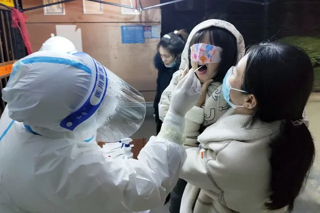 A medical worker wearing a protective suit swabs a child for a coronavirus test in Huaxian County in central China's Henan Province, Friday, January 14, 2022. China further tightened its anti-pandemic measures in Beijing and across the country on Friday as scattered outbreaks continued ahead of the opening of the Winter Olympics in a little over two weeks. (Photo by Chinatopix via AP Photo)