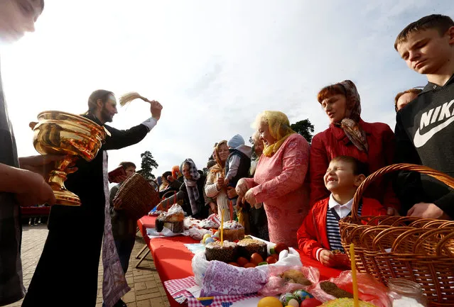 An Orthodox priest sprinkles holy water on believers and their “paskha” cakes, eggs and other food on the eve of Orthodox Easter outside the church in the town of Bobruisk, Belarus, April 30, 2016. (Photo by Vasily Fedosenko/Reuters)