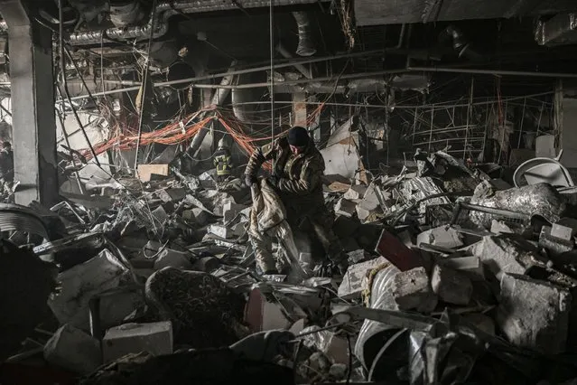 Ukranian servicemen search through rubble inside the Retroville shopping mall after a Russian attack in northwest of Kyiv on March 21, 2022. At least six people were killed in the overnight bombing of a shopping centre in the Ukrainian capital Kyiv, an AFP journalist said, with rescuers combing the wreckage for other victims. The 10-storey building was hit by a powerful blast that pulverised vehicles in its car park and left a crater several metres (yards) wide. (Photo by Aris Messinis/AFP Photo)