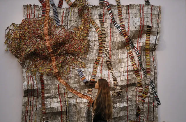A Sotheby's employee looks at a sculpture created by El Anatsui of Ghana at Sotheby's Modern and Contemporary African Art sale in London, Friday, May 12, 2017. The sculpture is estimated to fetch $810,000 to 1.06 million 650,000-850,000 pounds. (Photo by Frank Augstein/AP Photo)
