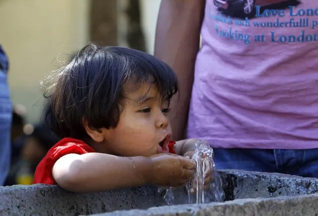 In this photo taken on Thursday, July 23, 2015 a girl, migrant from Afghanistan, tries to drink water near the railway station in the southern Macedonian town of Gevgelija. (Photo by Boris Grdanoski/AP Photo)