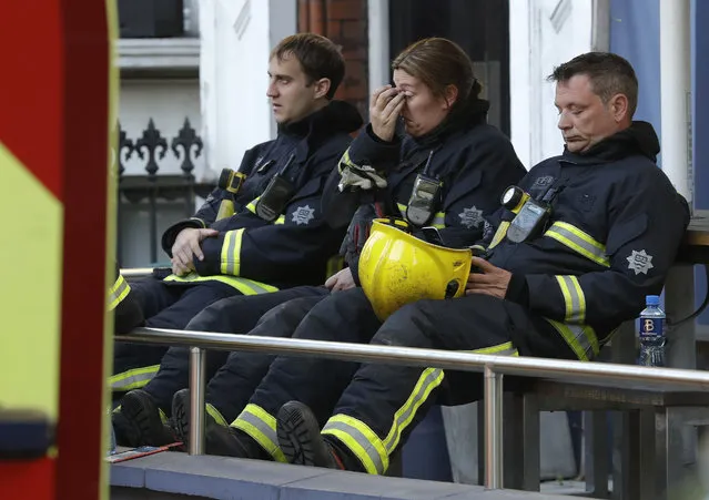 Firefighters wait to start their shift after a massive fire raged in a 27-floor high-rise apartment building in London, Wednesday, June 14, 2017. London's Metropolitan Police said a number of people were being treated for a range of injuries, but did not provide more specifics. London Mayor Sadiq Khan said on Twitter that a major incident had been declared. (Photo by Matt Dunham/AP Photo)